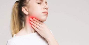 Boğazı ağrıyan genç bir kadın, boynunda iltihaplı bir bölgeye dokunuyor, boşluklu bir panorama.