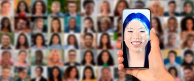Bir el, gülümseyen bir bireyle yüz taraması yapan bir akıllı telefonu tutuyor. Arka planda, çeşitli yüzlerden oluşan bir kolaj eylem halindeki modern tanımlama teknolojisini temsil ediyor..