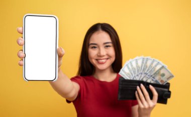 Uzun saçlı genç bir kadın bir elinde boş bir akıllı telefon, diğer elinde bir yığın para ile neşe içinde geziyor. Parlak sarı bir arka planda duruyor, heyecanla.