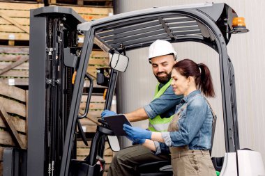Yükleme ürünleri yönetimi, modern cihaz ve kontrol sürücüleri depoda çalışıyor. Kasklı neşeli erkek elmaları kaldırıyor raflarda tahta sandıklarla, kadın kontrolörleri kaldırıyor.
