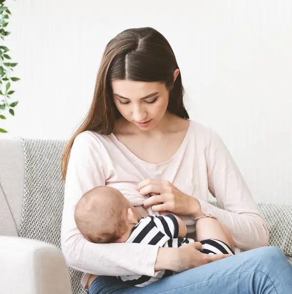 Emzirme kavramının önemi. Güzel anne yeni doğmuş çocuğunu anne sütüyle besliyor, evdeki kanepede oturuyor..
