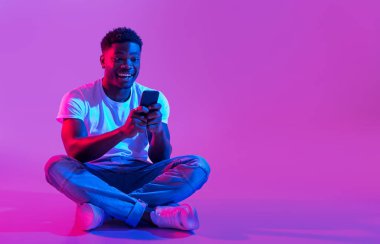 Bin yıllık Afro-Amerikan bir adam akıllı telefonuyla bacak bacak bacak üstüne atmış, sosyal medyada sörf yapıyor, neon ışıkta arkadaşlarıyla sohbet ediyor, mekanı kopyalıyor. Havalı siyah adam cep telefonu kullanıyor.