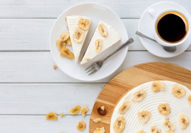 Tablo üstten görünüm üzerinde kahve fincanı ile lezzetli muz pasta. Meyve bisküvi ile karamel ve buttercream ahşap yemek tabağına dilimlenmiş, kopyalama alanı