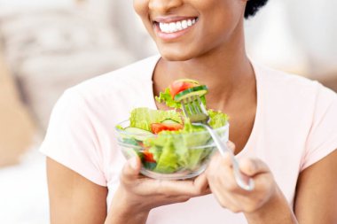 Kapalı alanda taze sebze salatası yiyen genç siyahi bir bayan manzarası. Afrikalı Amerikalı kadın zayıflama diyeti yapıyor, sağlıklı bir yaşam sürüyor, dengeli vejetaryen yemeği yiyor.