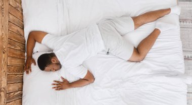 Hızlı uyuyan Afrikalı adam karnı üzerinde uyuyor evdeki yatak odasında huzur içinde dinleniyor. Dinlenme, dinlenme ve kestirme zamanı, derin erkek uyku konsepti. Üst Görünüm, Panorama