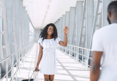 Önemseyen siyah adam havaalanında kız arkadaşıyla buluşuyor, mutlu kadın el sallıyor, sevgilisini boş yerde görmekten mutlu.