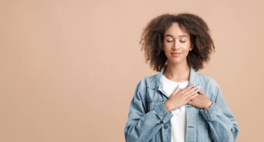 Minnettar ve umutlu bir kadının göğsünde el ele tutuşan portresi. Hoş kıvırcık kıvırcık, genç, Afro-Amerikan bayan. Kapalı gözlü, sarı arka planda izole edilmiş, boş alan, kesik, stüdyo çekimi.