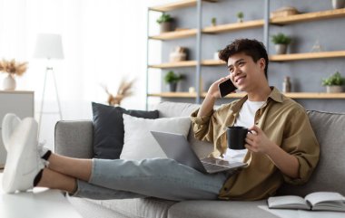 Neşeli Asyalı, serbest çalışan, kahve içen, cep telefonuyla konuşan, iş yerinde bilgisayar başında arkadaşlarıyla konuşan arkadaşlarıyla konuşan, koltukta dinlenen,