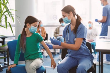 Coronavirus bağışıklığı, Covid-19 aşısı. Klinikte çocuk aşılayan doktor. Grip aşısı olan küçük bir kız. Çocuk doktoru çocuğu muayene ediyor ve iğne yapıyor. Corona virüsünün önlenmesi. Sağlık hizmetleri