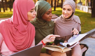 Şehir parkında oturmuş birlikte kitap okuyan üç Müslüman kadın. Modern Arap Kadın Öğrenciler Yaşam Tarzı, Üniversite Çalışması ve Eğitim Konsepti