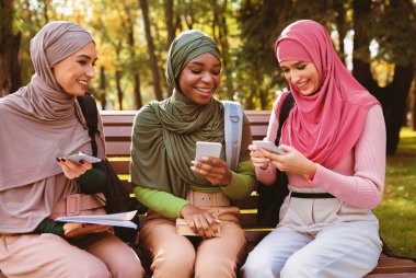 Bayan Müslüman Öğrenciler, dışarıda park yerinde oturmuş internetteki akıllı telefonları kullanarak interneti tarıyor. Sosyal medyada cep telefonlarıyla mesaj atan tesettürlü Arap kadınlar. Mobil Uygulama Kavramı