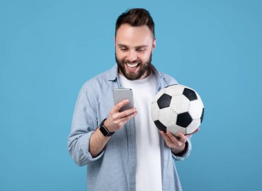 Futbol topu kullanan, akıllı telefon kullanan, spor bahsini kazanan, mavi stüdyoda en sevdiği takımı destekleyen genç adam. Milenyum adamı çevrimiçi futbol şampiyonasını izliyor