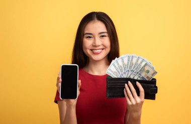 Neşeli bir yüzü olan bir kadın bir elinde akıllı bir telefon, diğer elinde para dolu bir cüzdan, parlak sarı bir arka plana karşı, finansal başarı duygusunu ön plana çıkarıyor..