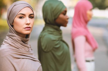 Üç farklı müslüman kadının başörtüsü takmış, park yerinde sıraya girmiş, başörtüsü takmış şekilde yan yana duran grup portresi. İslam Kadın Çeşitliliği ve Eşitlik Konsepti. Seçici Odaklanma.