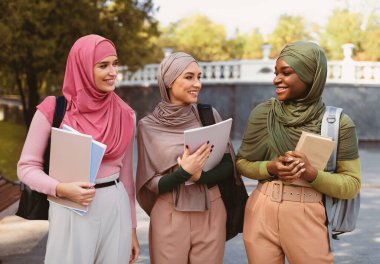 Türban takmış üç Müslüman kız öğrenci açık havada parkta kitap tutuyorlar. Modern Arap Kadınları İçin Eğitim, Yurtdışında Üniversite Çalışması, Mutlu İslami Öğrenci Konsepti