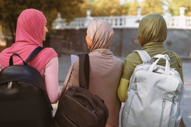 Sırt çantalı üç tanınmayan Müslüman öğrenci parktaki kameraya doğru yürüyorlar. Modern Arap Kadın Konsepti için Üniversite Eğitimi ve Yaşam Tarzı, Eğitim ve Derece. Arka Görünüm