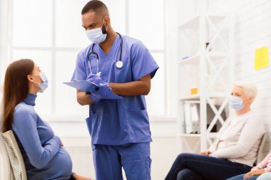 Coronavirus salgını sırasında doktor randevusu. Erkek hemşire, hastanede hamile bir kadınla konuşuyordu. Tıbbi Tedavi, Covid-19 Salgın Konsepti. Seçici Odaklanma