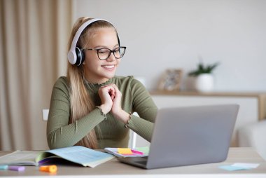E-eğitim, çevrimiçi dersler ve öğrenciler için kurslar. Kulaklıklı neşeli sarışın kız dizüstü bilgisayara bakıyor, online ders izliyor ya da özel hoca dinliyor, iç mekan kopyalıyor.
