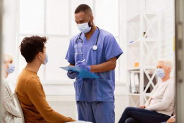 Coronavirus Tıbbi Geçmişi. Siyahi doktor, Asyalı hasta adamla hastanenin bekleme odasındaki hastalık belirtileri hakkında konuşuyor. Corona Virüs Salgını Konsepti. Boş Alan