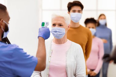 Coronavirus, Covid-19 Koruma. Sıcaklık taraması yapan Sıcaklık İşçisi Kıdemli Hanımları Kızılötesi Temassız Themometre ile Alnını Tarıyor, İçerideki İnsanlar İçin Ateşi Ölçüyor