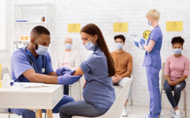 Coronavirus aşısı. Afro-Amerikalı doktor hastanede çalışan hamile bayana Covid-19 aşısı yapıyor. Corona Virüs Nüfus Bağışıklık Kampanyası Reklamları. Boşluğu Kopyala