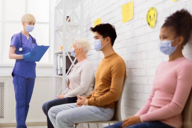 Coronavirus tedavisi. Muhtelif insanlar sırada oturup doktor randevusu bekliyor, hemşire hastalarla hastane bekleme odasında konuşuyor. Covid-19 Tıbbi Yardım ve Aşı. Seçici Odaklanma