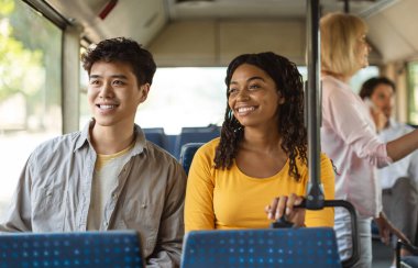 Otobüs koltuğunda oturan mutlu, çoklu etnik çeşitliliğe sahip bir çiftin portresi. Pencereden dışarı bakan gülümseyen siyahi kadın ve Asyalı adam. Kamu aracıyla gezmekten ya da gezmekten keyif alıyorlar.