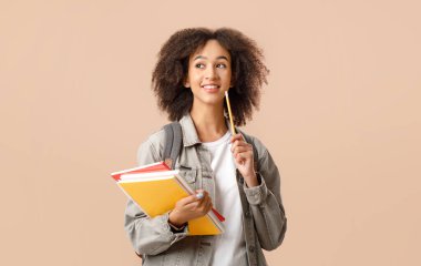 Modern eğitim, üniversite ve öğrenci duyguları. Sırt çantası ve not defterleri olan düşünceli Afrikalı Amerikalı kadın elinde kalemle arka planda izole edilmiş boş alana bakıyor.