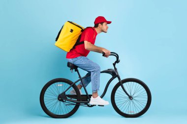Yemek teslimatı. Kurye Adam 'ın sarı sırt çantalı bisiklete binerken yandan görünüşü paket kahve ya da restorandan yemek teslimatı, Stüdyo Çekimi. Teslimatçı Hizmet Konsepti