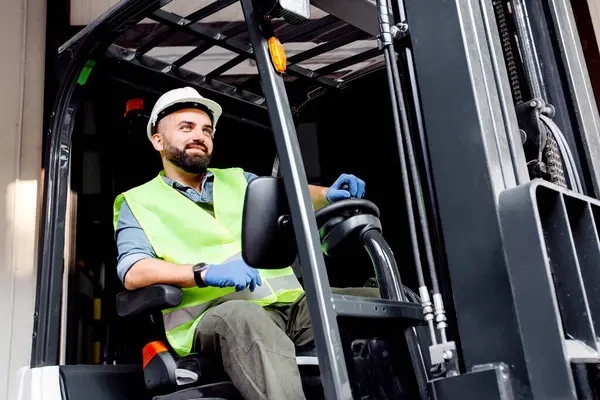 Depoda çalışıyorum, organik meyveleri satıyorum ve meyve suyu üretiyorum. Kasklı gülümseyen adam forklift kamyonuyla depodaki kırmızı olgun elmalarla dolu ahşap konteynırı kaldırıyor.