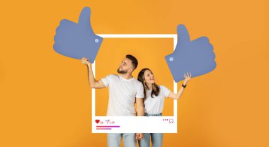 Bir çift birlikte duruyor, her birinin elinde parlak turuncu bir arka plana karşı büyük parmakları var. Çevrimiçi içeriği ve sosyal medya etkileşimini desteklemek için heyecanlı görünüyorlar.