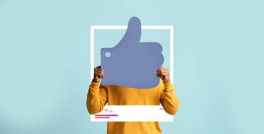 Sarı kazak giyen bir kişi açık mavi bir arkaplana karşı büyük bir başparmak kaldırma ikonu tutar. Sosyal medya platformlarında etkili olarak pozitif katılımı kutluyorlar.