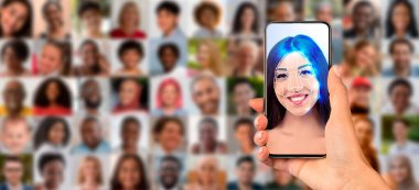 Bir el, modern yüz tanıma teknolojisini vurgulamak için yüz taraması yapan bir akıllı telefonu tutuyor. Arka planda çok sayıda portre bulanık, çeşitli bireyler sergileniyor.