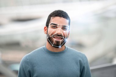 Yüz tanıma teknolojisi özelliklerini incelerken bir adam dışarıda gülümsüyor. Bu, çeşitli ayarlardaki yeni tanımlama süreçlerini yansıtır.