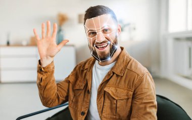 Çağdaş bir ofiste oturmuş, yüz tanıma teknolojisini gösteren bir adam el sallıyor. Oda aydınlık ve minimalisttir. Kimlik saptamaya modern bir yaklaşımı yansıtır..