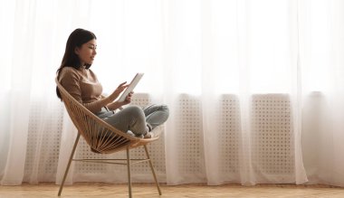 Tembel hafta sonu. Tablet kullanan kız, pencereye karşı hasır sandalyede oturan, boş alanı olan panorama