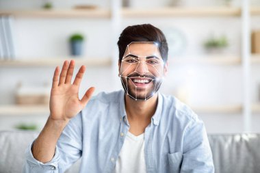Hintli adam yüz tanıma teknolojisini ev ortamında kullanıyor. El sallarken gülümsüyor, dijital bir örtüyle yüz hatlarını belirtiyor..