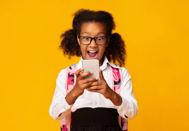 Heyecanlı Siyah Okul Kızı Sarı Stüdyo Arkaplanda Akıllı Telefon Kullanıyor. Çocuklar ve Telefon Bağımlılığı. Boş Alan