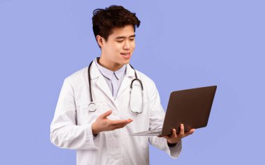 Çevrimiçi Danışmanlık Hizmetleri Konsepti. Kendine güvenen Asyalı erkek doktorun portresi dizüstü bilgisayar kullanıyor, video sohbet sırasında hastayla konuşuyor, mavi stüdyoda tek başına duruyor, kopyalama uzayı. Teletıp