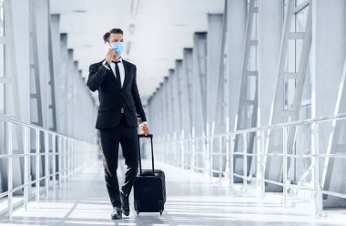 Zengin girişimci, havaalanının önünden bavulla geçerken telefonla konuşuyor.