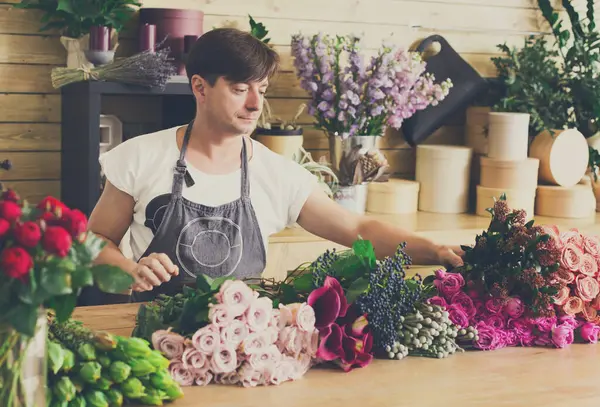 Çiçek teslimatçısı. Çiçek buketi yapan bir çiçekçi. Çiçek tasarım stüdyosunda dekorasyon ve düzenlemeler yapan bir erkek asistan ya da mal sahibi. Düzen oluşturuluyor