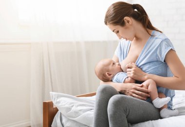 Yemek zamanı. Anne bebeğini emziriyor, evde yatakta oturuyor, boş yer var.