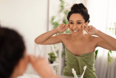 Evdeki aynanın yanında lenfatik drenaj yüz masajı yapan güzel genç bir kadın. Boş yer. Güzel bir milenyum kadını banyoda cilt bakımı yapıyor.