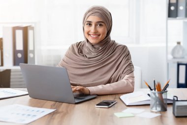 Müslüman Kadınlar İçin Modern İş. Ofiste dizüstü bilgisayarda çalışan mutlu İslamcı kız portresi ve kameraya bakmak, boşluğu kopyalamak