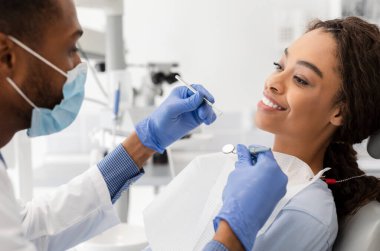 Afrikalı genç bir kadın dişçiye gidiyor, maskeli ve eldivenli doktor kontrol ediyor, yandan bakıyor, kapatıyoruz.