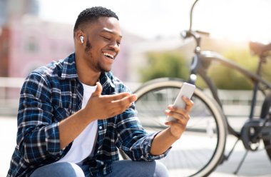 Modern İletişim. Neşeli, mutlu Afrikalı adam akıllı telefondan video görüşmesi yapıyor, arkadaşlarıyla konuşuyor ve el kol hareketi yapıyor.