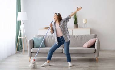 Oturma odasında yerleri silerken şarkı söyleyen, mikrofon olarak paspası kullanan ev işleri yaparken eğlenen mutlu genç bir kadın. Milenyum hanımefendisi ev işlerinden zevk alıyor, temizlik yapıyor.