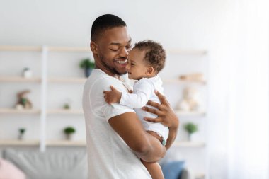 Genç siyahi baba ve bebeğin evde birbirine bağlandığı, Afrika kökenli Amerikalı babanın sevimli bebeğini kucağına alıp gülümsediği, babalık izninin keyfini çıkardığı, boşluğu kopyaladığı portresi.