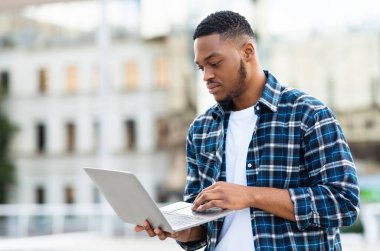 Bilgi ve Teknoloji Konsepti. Odaklanmış Afrikalı adam dışarıda dizüstü bilgisayar tutuyor, seçici odaklı.