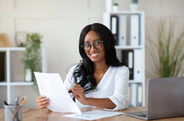 Ofisteki evraklarla çalışan güzel siyahi iş kadını. Afrika kökenli Amerikalı kadın girişimci işyerinde önemli bir sözleşme ya da anlaşma arıyor